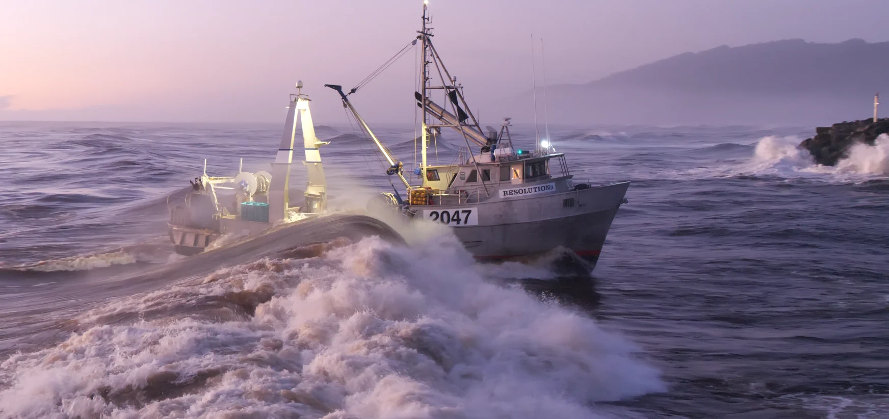 Vessel Resolution II crossing the Greymouth bar at dusk, spray flying, mountains behind