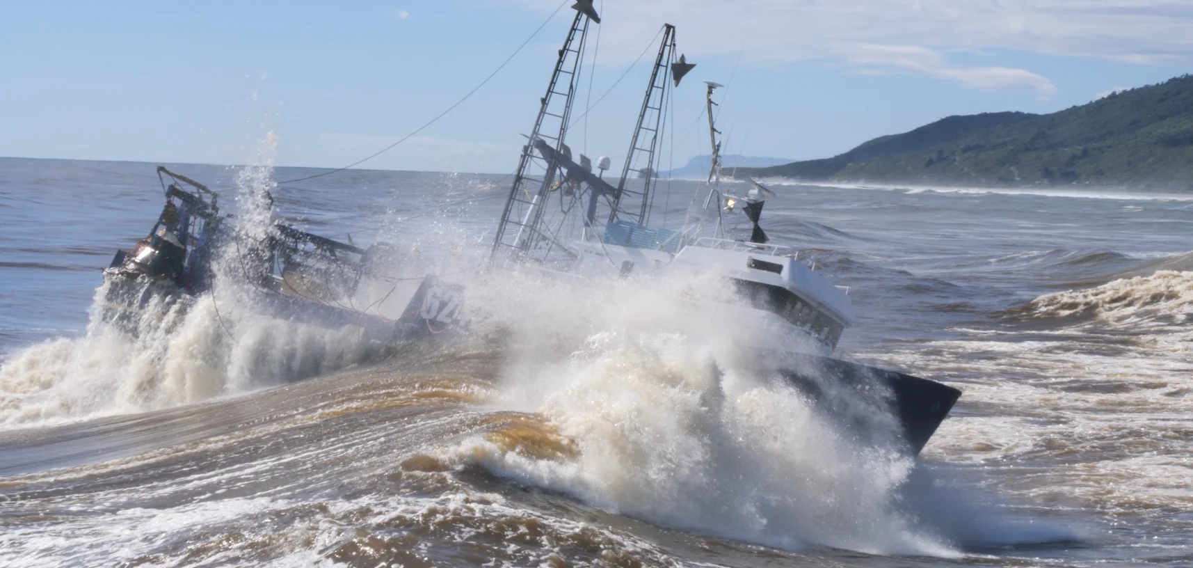 Two vessels crossing the Greymouth bar simultaneously, massive spray and blue sky behind